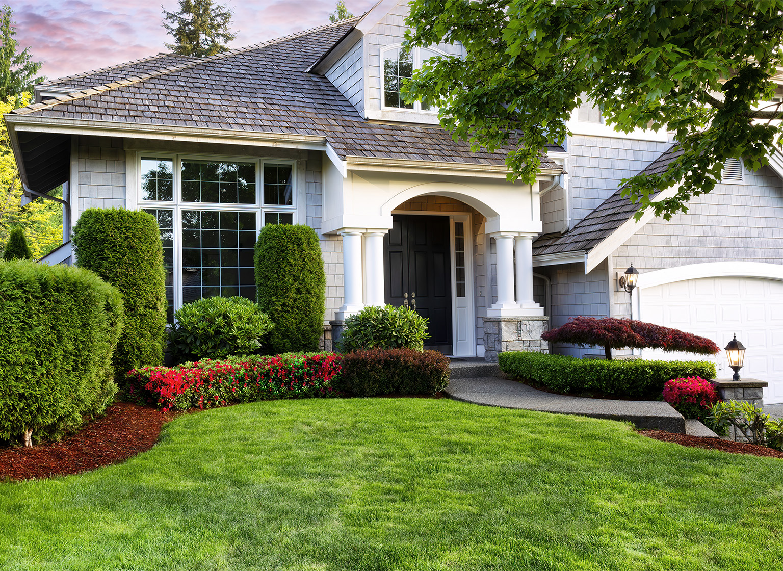 Beautiful home exterior in evening with manicured green lawn and blooming red flowers in bushes